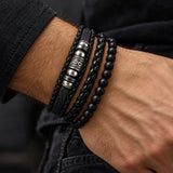 Man wearing a SEYOR three-piece black bracelet set with braided leather, engraved silver-tone details and matte black beads.