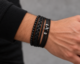 Man wearing a SEYOR black multi-layer bracelet set with matte beads, braided leather and a silver-tone crossed-arrows detail.