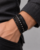 Man wearing a SEYOR black multi-layer bracelet set with faceted beads, braided leather bands and silver-tone stud details.