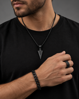 Man wearing a SEYOR black arrowhead necklace, Cuban chain bracelet and engraved band ring with a black shirt.