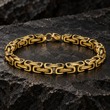 Close-up of a men’s gold-tone Byzantine link bracelet displayed on a rugged dark stone surface.