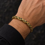 Man wearing a gold-tone stainless steel Byzantine link bracelet with dark accents and an intricate geometric design.