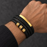 Man wearing a SEYOR multilayer black leather bracelet with braided strands, polished gold-tone bar, gold spacers and magnetic clasp.