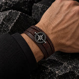 Man wearing a multilayer brown leather bracelet with braided detailing and a silver-tone compass medallion.