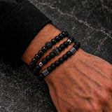 Man wearing three stacked SEYOR black beaded bracelets with polished and matte finishes, crown charm and gunmetal spacers.