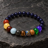 Close-up of SEYOR men's multicolor planet bracelet with dark blue galaxy-style beads on a black stone background