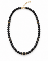 Men’s matte black onyx bead necklace with square lava stone accents, gold-tone spacers and an adjustable chain on white.