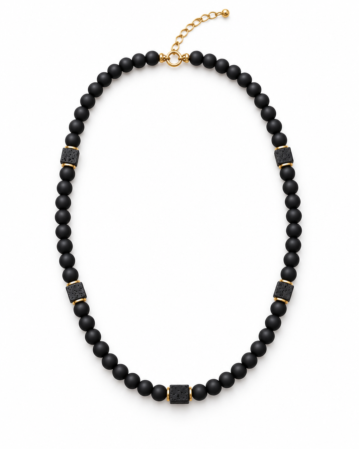 Men’s matte black onyx bead necklace with square lava stone accents, gold-tone spacers and an adjustable chain on white.