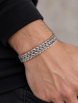Close-up of a male wrist wearing a wide polished silver-tone woven chain bracelet.