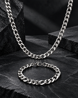 Men’s silver Cuban link necklace and matching bracelet arranged on a rugged black stone surface.