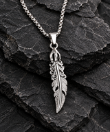 Detailed silver-tone feather pendant necklace arranged on rugged black stone.