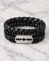 Front view of a men’s black layered bracelet set featuring a silver-tone razor blade centerpiece